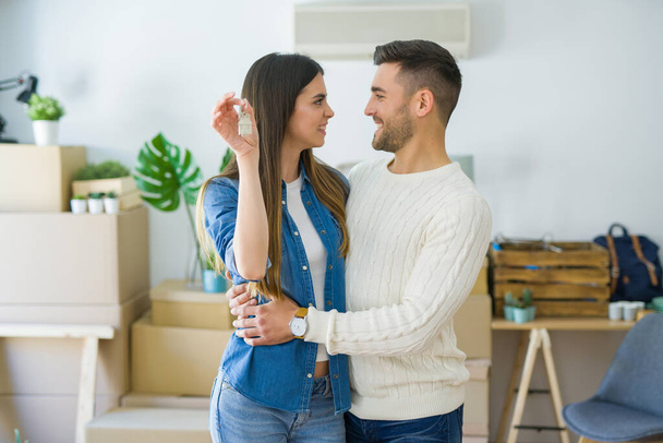 Young couple moving to a new home, hugging in love showing keys of new apartment smiling very happy - Foto, imagen