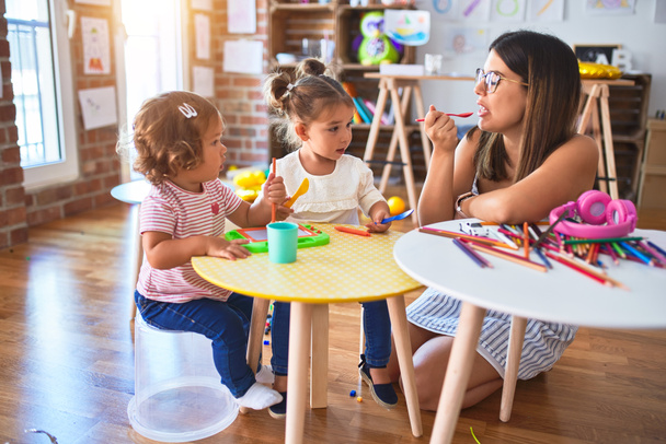 junge schöne Lehrerin und Kleinkinder spielen Mahlzeiten mit Plastiknahrung und Besteck Spielzeug im Kindergarten - Foto, Bild