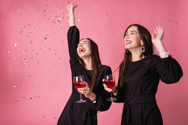 Two women celebrate the New Year party having fun laughing under the flying confetti and drinking wine. - Photo, Image