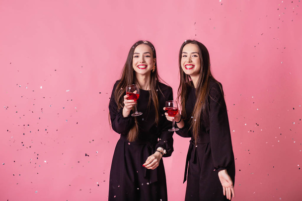Twee vrouwen vieren het nieuwjaarsfeest met plezier lachen onder de vliegende confetti en wijn drinken. - Foto, afbeelding
