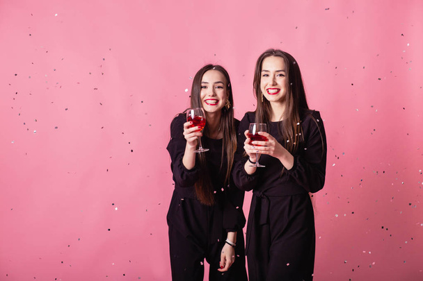 Dos mujeres celebran la fiesta de Año Nuevo divirtiéndose riendo bajo el confeti volador y bebiendo vino
. - Foto, Imagen