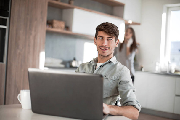 young man sitting in front of open laptop in kitchen - Foto, Imagen