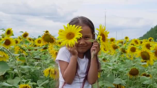 Μάτια ηλιοτρόπια. Αξιολάτρευτο μικρό κορίτσι κρατώντας ηλιοτρόπια στα μάτια σαν κιάλια στον κήπο. Κοντινό πλάνο για παιδιά, το μωρό κλείνει τα μάτια της με δύο ηλιοτρόπια. - Πλάνα, βίντεο