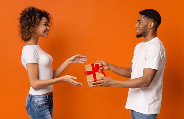 Cheerful african man giving holiday gift to girlfriend - Foto, Bild