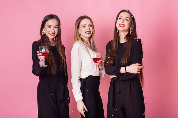 Τρεις γυναίκες γιορτάζουν την Πρωτοχρονιά διασκεδάζοντας γελώντας κάτω από τα ιπτάμενα κομφετί και πίνοντας κρασί.. - Φωτογραφία, εικόνα