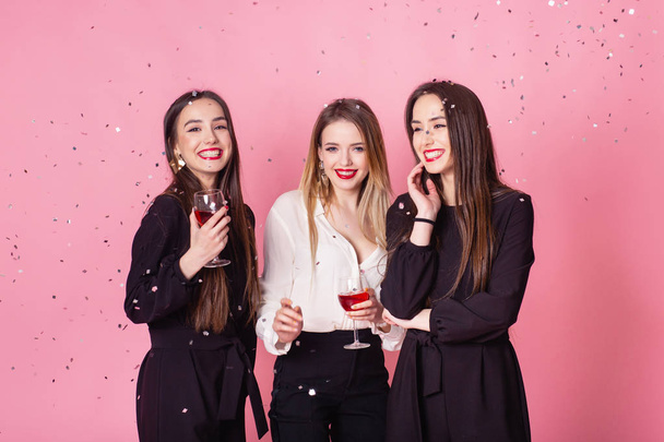 Kolme naista juhlii uudenvuoden juhlia hauskaa nauraen lentävän konfettin alla ja juoden viiniä.
. - Valokuva, kuva