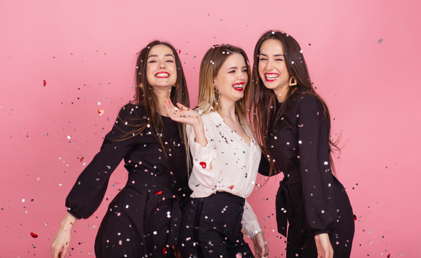 Tres mujeres celebran la fiesta de Año Nuevo divirtiéndose riendo bajo el confeti volador
. - Foto, imagen