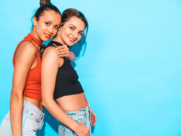 Two young beautiful smiling brunette hipster girls in trendy similar summer colorful shirt clothes.Sexy carefree women posing near blue wall in studio.Positive models having fun - Fotografie, Obrázek
