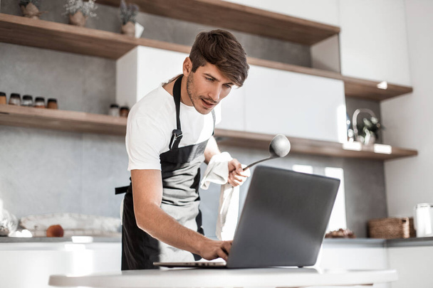 young man looking at laptop screen while cooking dinner - Foto, immagini