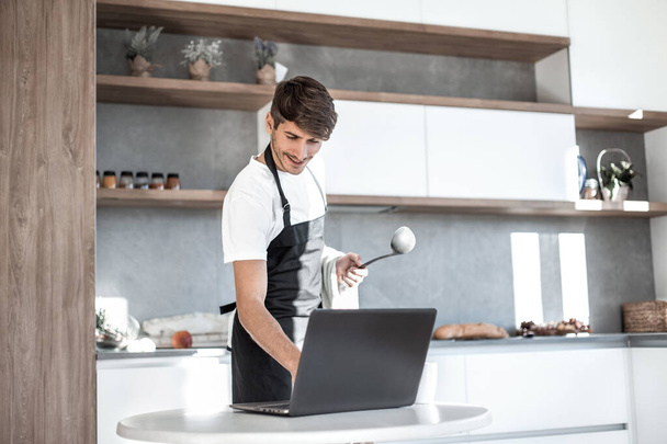 young man looking at laptop screen while cooking dinner - Foto, afbeelding