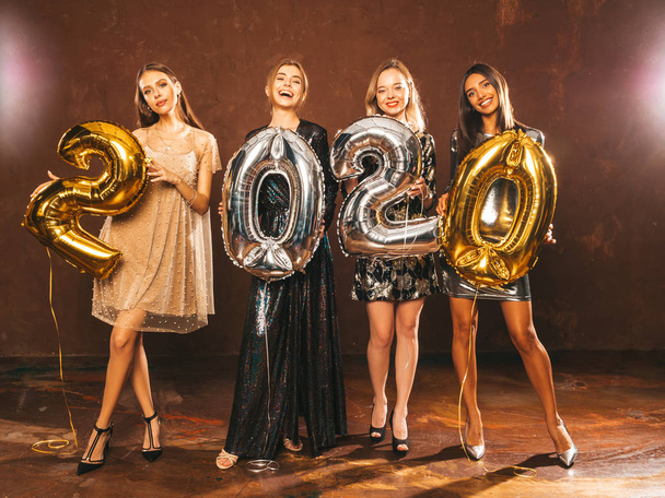 Прекрасні жінки святкують Новий рік. Щасливі чудові дівчата в стильних сексуальних вечірніх сукнях тримають золоті та срібні кулі 2020 року, розважаючись на новорічній вечірці. Святкування свята. Чарівні моделі
  - Фото, зображення