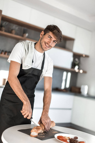 smiling man in an apron, slicing the bread for sandwiches - Foto, immagini