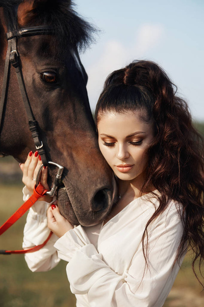 Meisje in een lange jurk staat naast een paard, een mooie vrouw stro - Foto, afbeelding