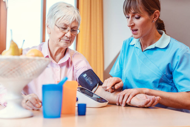 Медсестра вимірює кров'яний тиск на старшу жінку
 - Фото, зображення