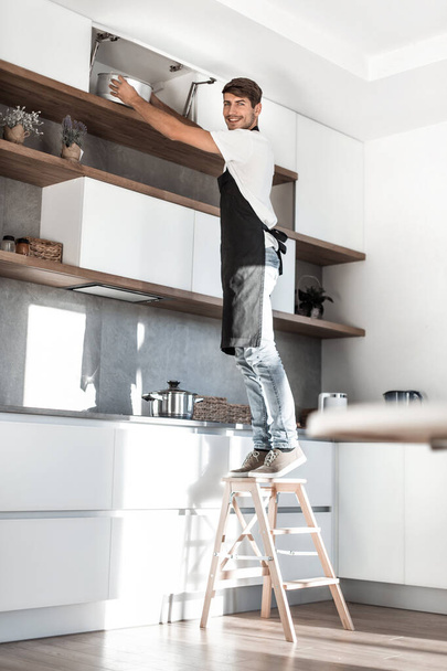 man standing on a stepladder in the home kitchen - Foto, afbeelding
