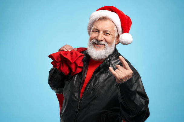 Happy mature man wearing Santa hat showing double horn sign - Foto, afbeelding