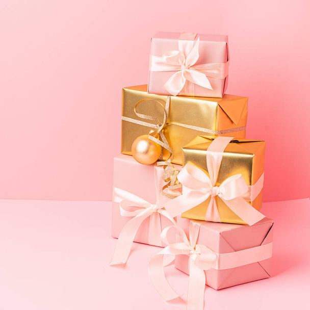 Святкові золотисто-рожеві коробки з іграшковими кульками з атласною стрічкою на пастельно-рожевому тлі. Концепція свята
. - Фото, зображення