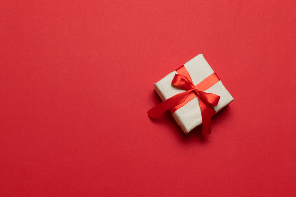 Caja regalo o regalo con lazo de cinta roja en la vista superior de la mesa roja. Composición de moda para cumpleaños, día de la madre o boda
. - Foto, imagen