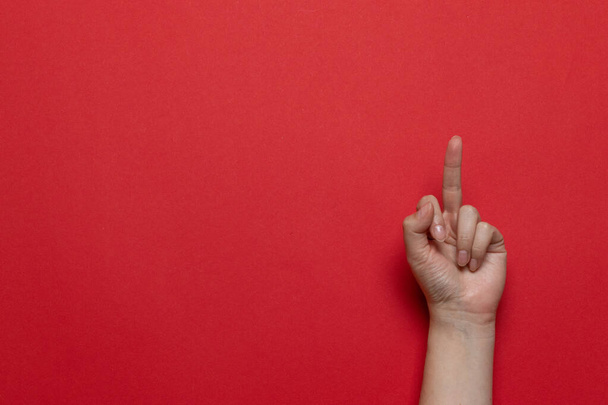Mano de mujer mostrando el dedo medio sobre un fondo rojo. Composición plana estilo laico
 - Foto, Imagen
