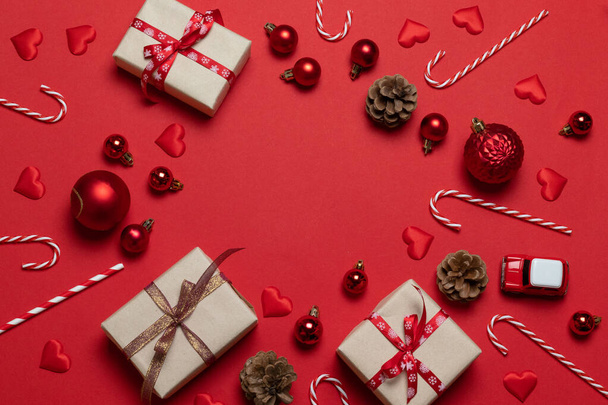 Χριστουγεννιάτικο και Πρωτοχρονιάτικο πανό διακοπών με craft δώρο, αυτοκίνητο και κουκουνάρια έλατο σε κόκκινο φόντο. Επίπεδο lay, πάνω όψη - Φωτογραφία, εικόνα
