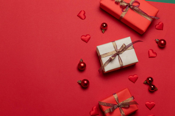 Christmas composition of surprise boxes decorated with shiny ribbons, red Christmas balls, heart shapes on a red background - Photo, Image