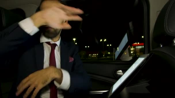 Serious businessman working on tablet at night in the back seat of his limousine with personal driver - Footage, Video