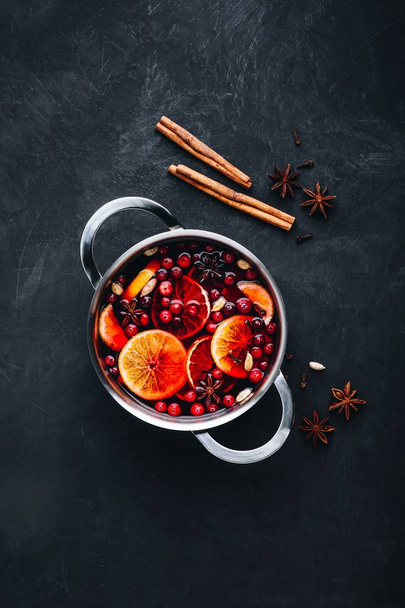 Glühwein Hot Drink met Cranberries, sinaasappels, appels en specerijen op donkere betonnen ondergrond.  - Foto, afbeelding