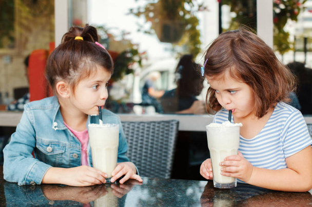 Két vicces kaukázusi kisiskolás testvér tejet iszik a kávézóban. A barátok jól érzik magukat együtt. Hideg nyári desszertek gyerekeknek. Boldog autentikus gyermekkori életstílust.  - Fotó, kép