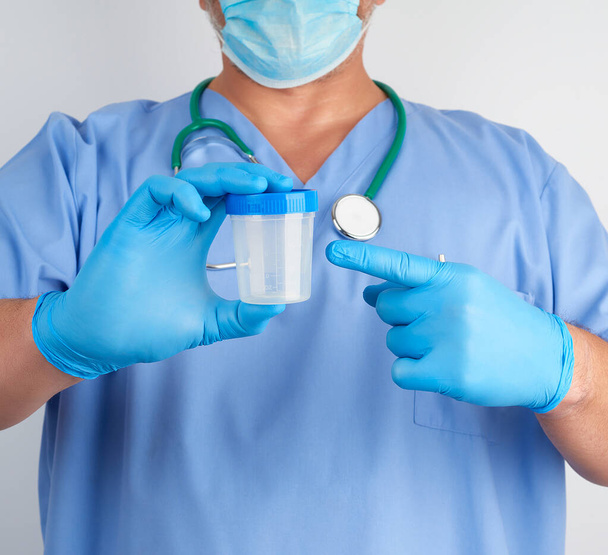 doctor in blue uniform and latex gloves is holding an empty plas - Фото, изображение