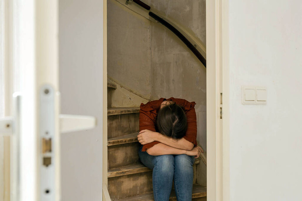 Üzgün kadın tek başına oturuyor ve merdivenlerde ağlıyor, evin tadilata, inşaata ve yenileme konseptine ihtiyacı var. - Fotoğraf, Görsel