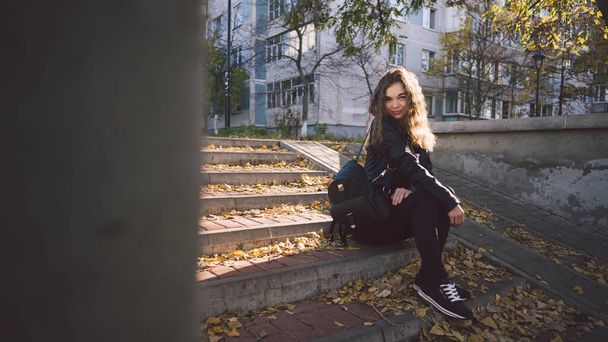 A young beautiful woman in casual clothes is sitting on the steps with leaves in the urban district. - Foto, immagini