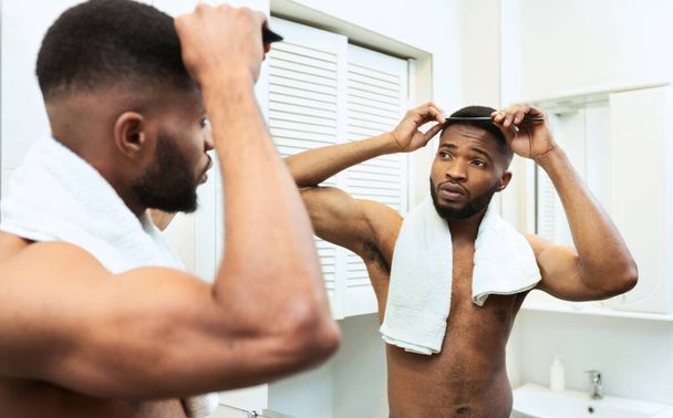 Harika Afrikalı Amerikalı adam banyoda saçını tarıyor. - Fotoğraf, Görsel