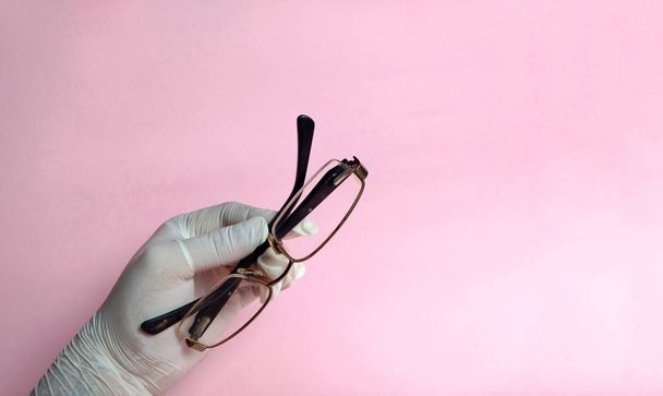 Ruka s bílou rukavicí s brýlemi na růžovém pozadí. lékařské pojetí. optická skla - Fotografie, Obrázek
