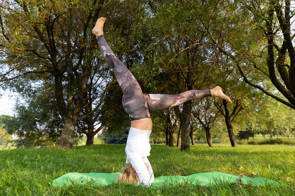 Chica de pie sobre su cabeza mientras hace yoga en el parque
 - Foto, Imagen