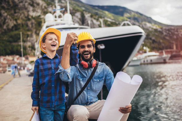 Ingeniero de puerto con su hijo sosteniendo el papel, la varita de construcción
 - Foto, Imagen