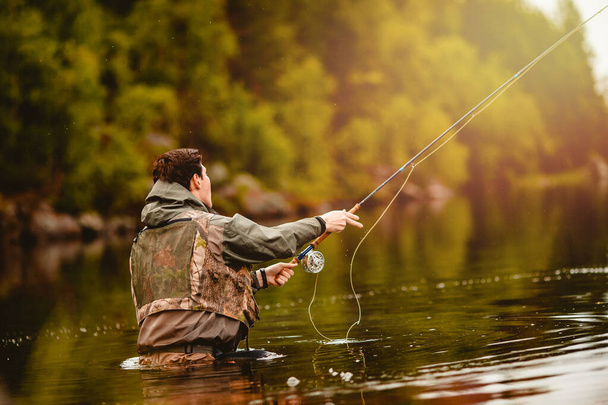 Рыбак с помощью палочной мухи ловит рыбу в горной реке - Фото, изображение