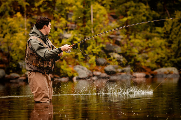 Рыбак с помощью палочной мухи ловит рыбу в горной реке - Фото, изображение