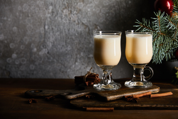 glasses with delicious eggnog drink on cutting board near spruce branch on grey stone background - Foto, afbeelding