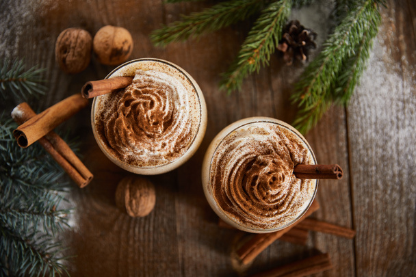 top view of delicious eggnog drink near spruce branches, wallnuts and cinnamon sticks on wooden table - Zdjęcie, obraz