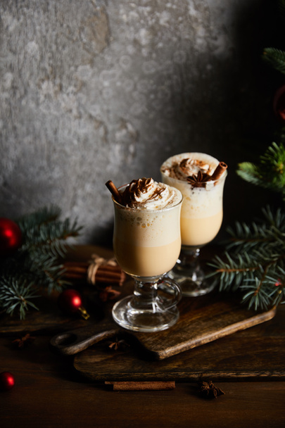 delicious eggnog cocktail with whipped cream and cinnamon on cutting board near spruce branches on grey stone background - Photo, Image