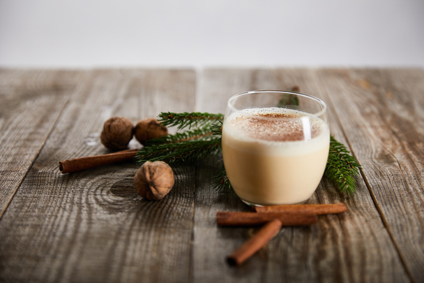 delicious eggnog cocktail near wallnuts, spruce branch and cinnamon sticks on wooden table isolated on grey - Photo, Image