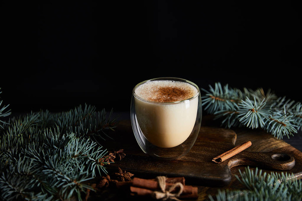 delicious eggnog cocktail on cutting board near spruce branches and cinnamon sticks isolated on black - Foto, immagini