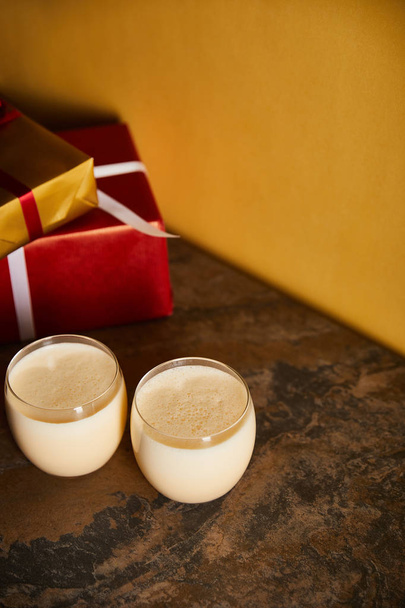 delicious eggnog cocktail and gift boxes on dark marble table near orange wall - Photo, Image