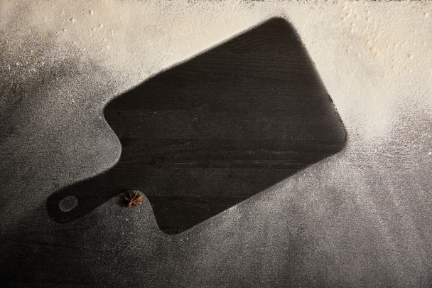 πάνω όψη μαύρης πλάκας κοπής και αστεροειδούς γλυκάνισου σε τραπέζι καλυμμένο με ζάχαρη σε σκόνη - Φωτογραφία, εικόνα