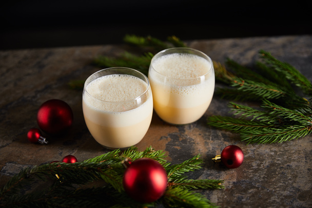 delicious eggnog cocktail, spruce branches and christmas balls on dark marble table isolated on black - Foto, imagen