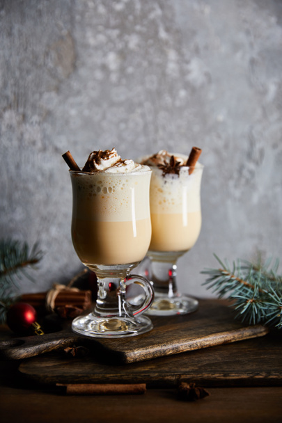 traditional eggnog cocktail with whipped cream and cinnamon on cutting board near spruce branches on grey stone background - Foto, imagen