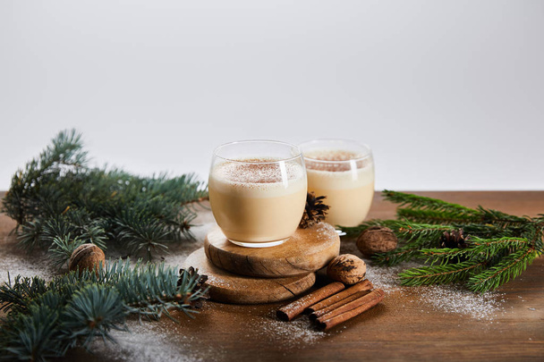 flavored eggnog cocktail on round boards, spruce branches, cinnamon sticks and walnuts isolated on grey - Photo, Image