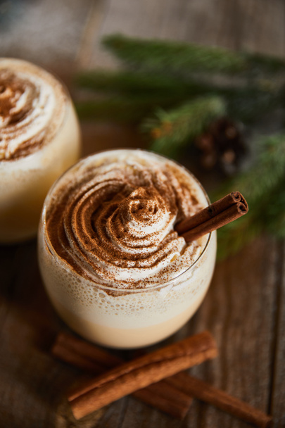 close up view of delicious eggnog cocktail with whipped cream and cinnamon on wooden table - Foto, imagen