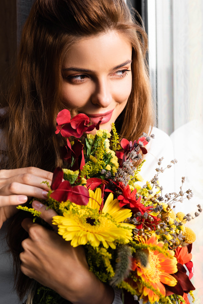 smiling redhead woman with bouquet of autumn flowers near window  - Zdjęcie, obraz