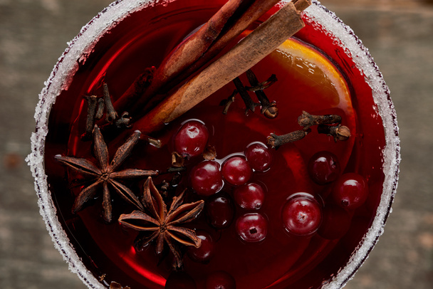vrchní pohled na červeně kořeněné svařené víno s bobulemi, anýzem, pomerančovými plátky a skořicí ve skle zdobené cukrem - Fotografie, Obrázek